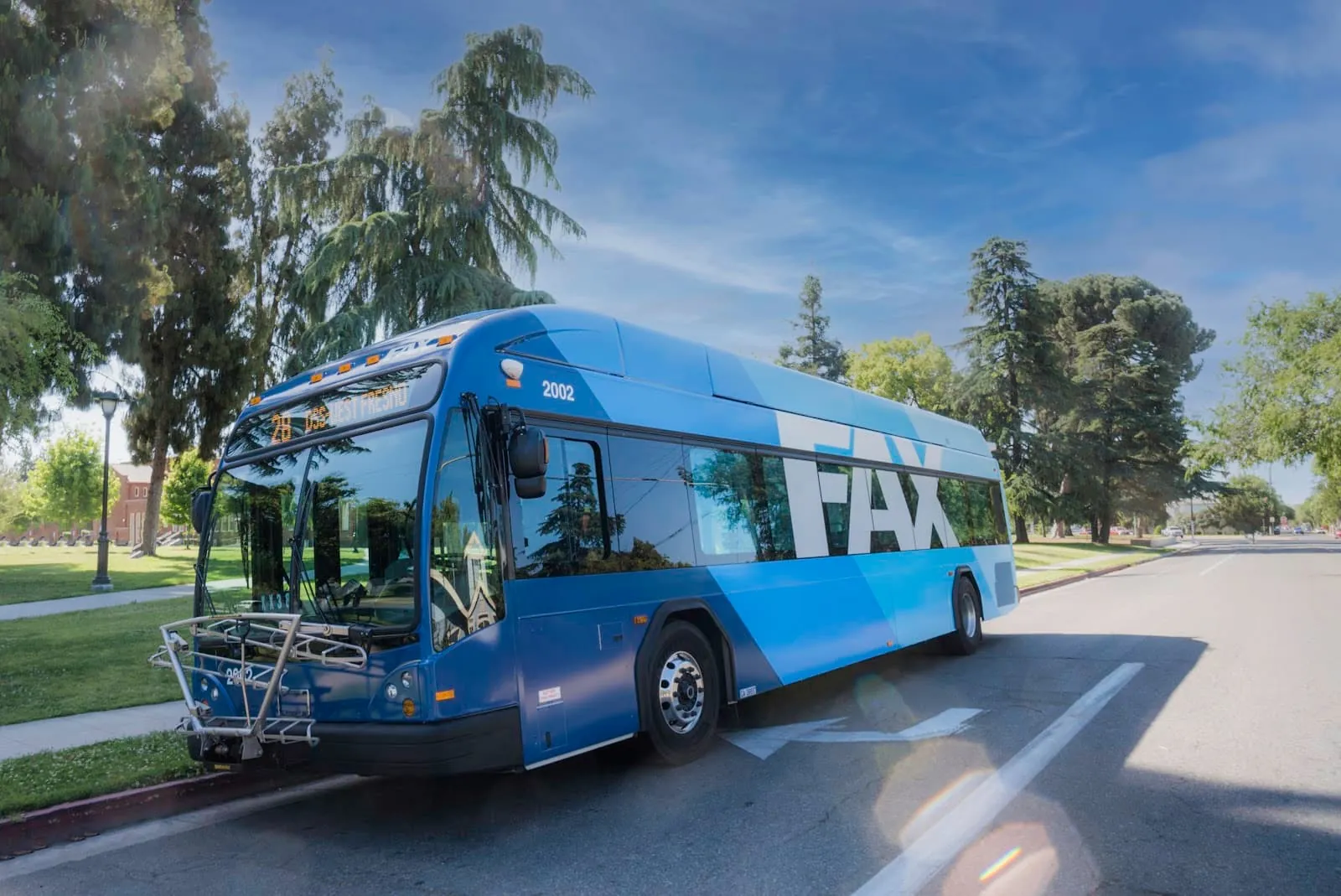 A blue FAX bus parked on a tree-lined Fresno street